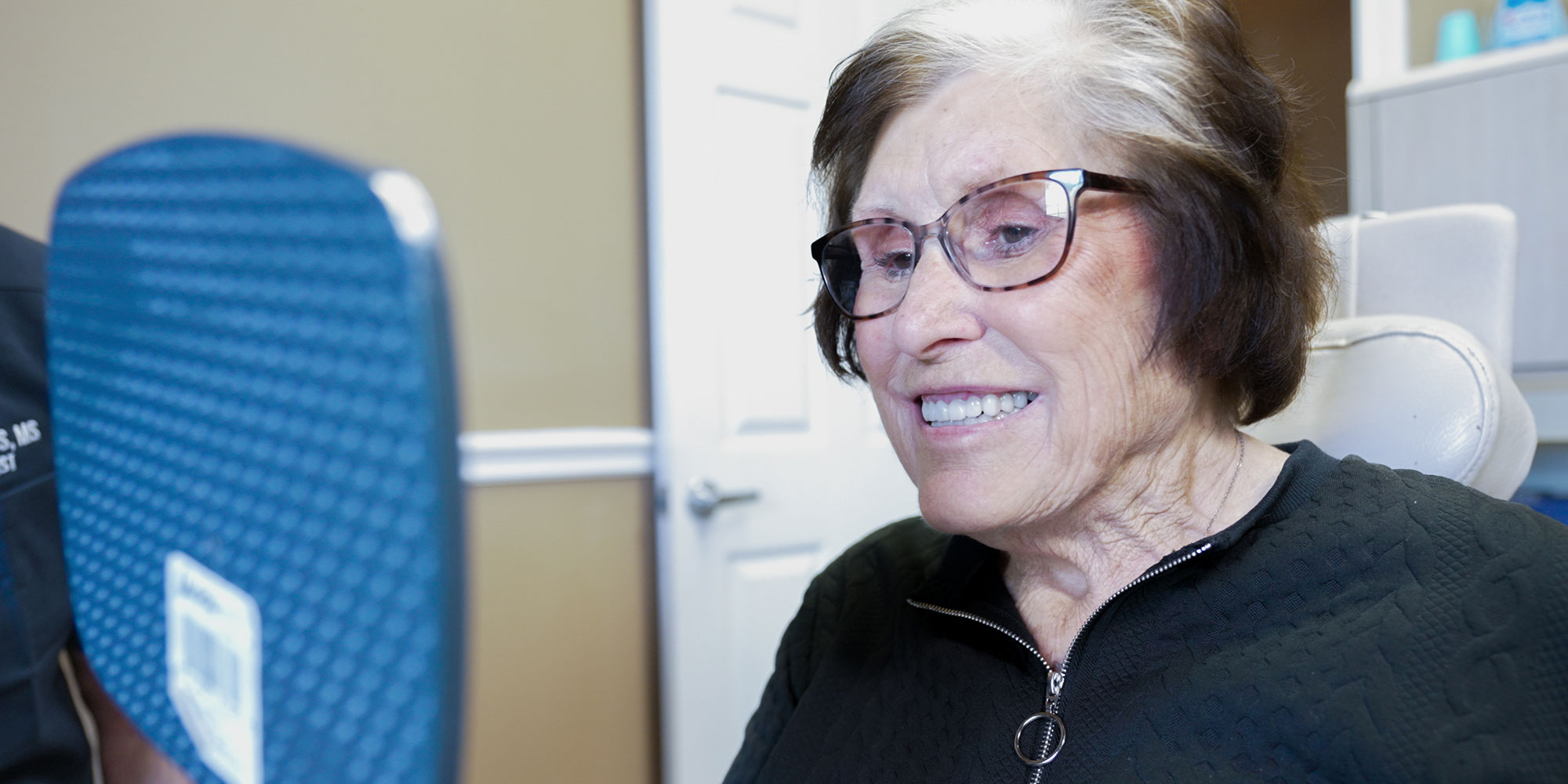 lady with glasses smiling with mirror after full arch dental implants